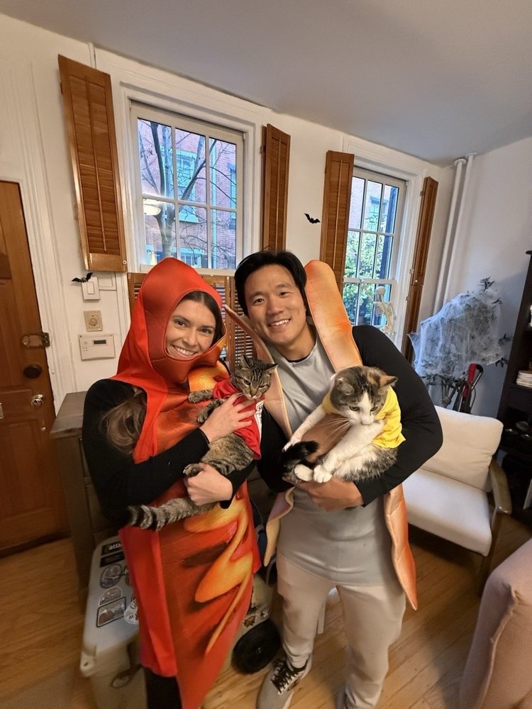 Andy and Paige at home in Halloween costumes, each holding one of their two cats